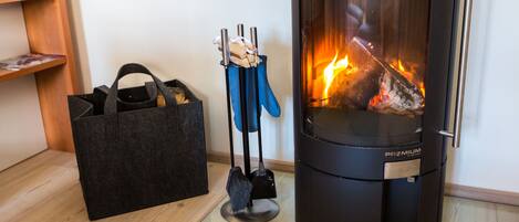 A wood-burning stove with a glass door, a black bag, and a blue dustpan and brush on the floor.