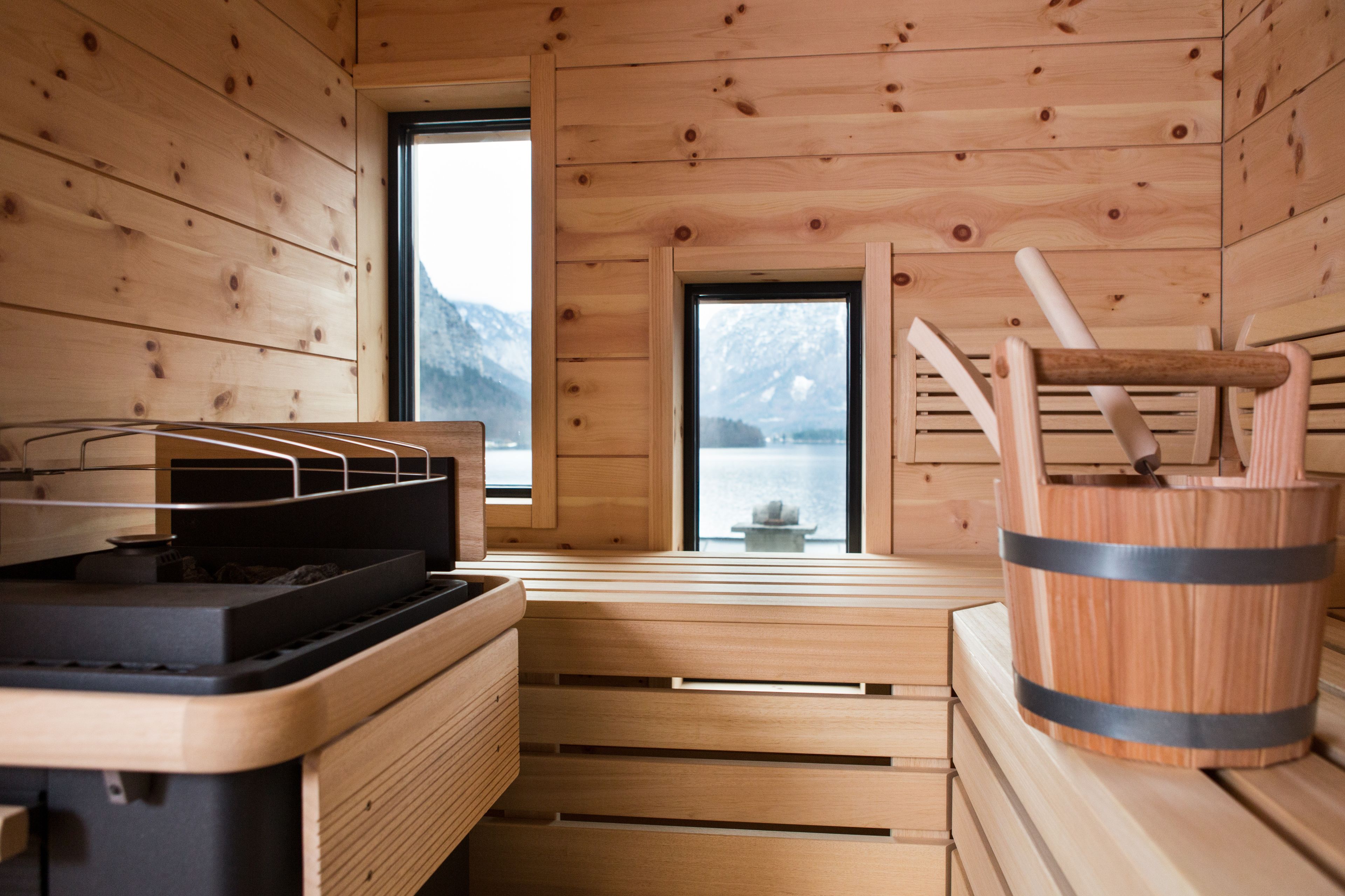 Een houten sauna met een bank, een emmer en een raam met uitzicht op bergen.