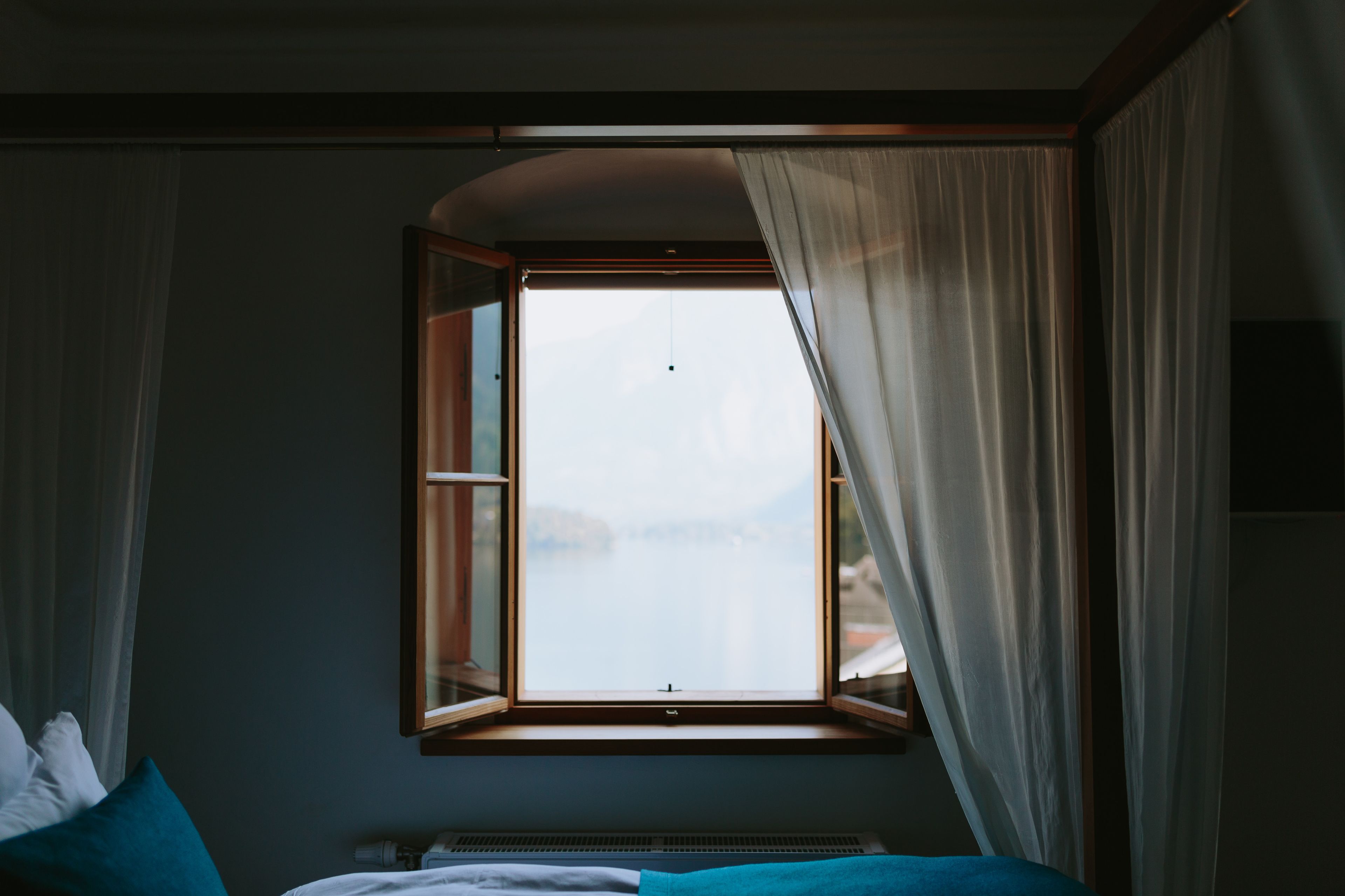 A room with a bed, a window with curtains, and a view of the outside.