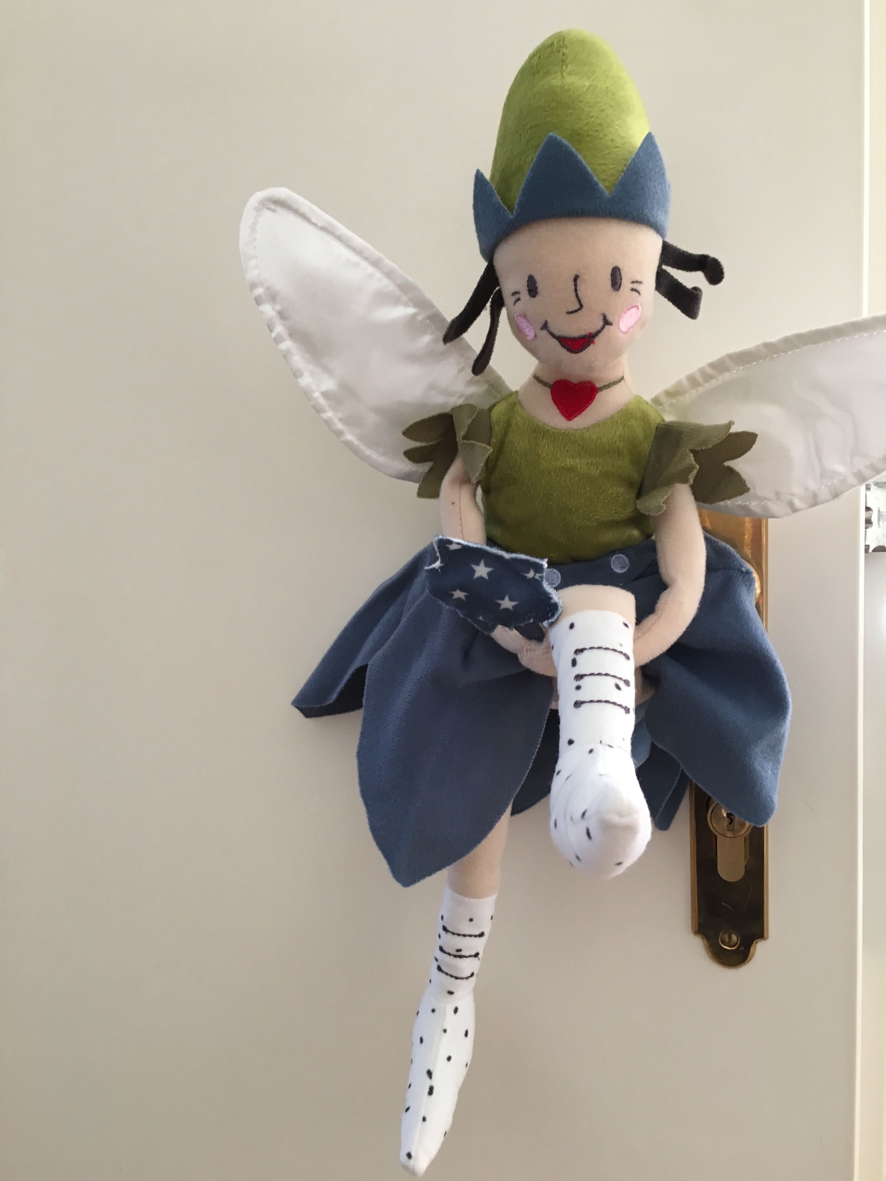 Un jouet en peluche avec des ailes et un nœud papillon rouge, posé sur une étagère fixée au mur.