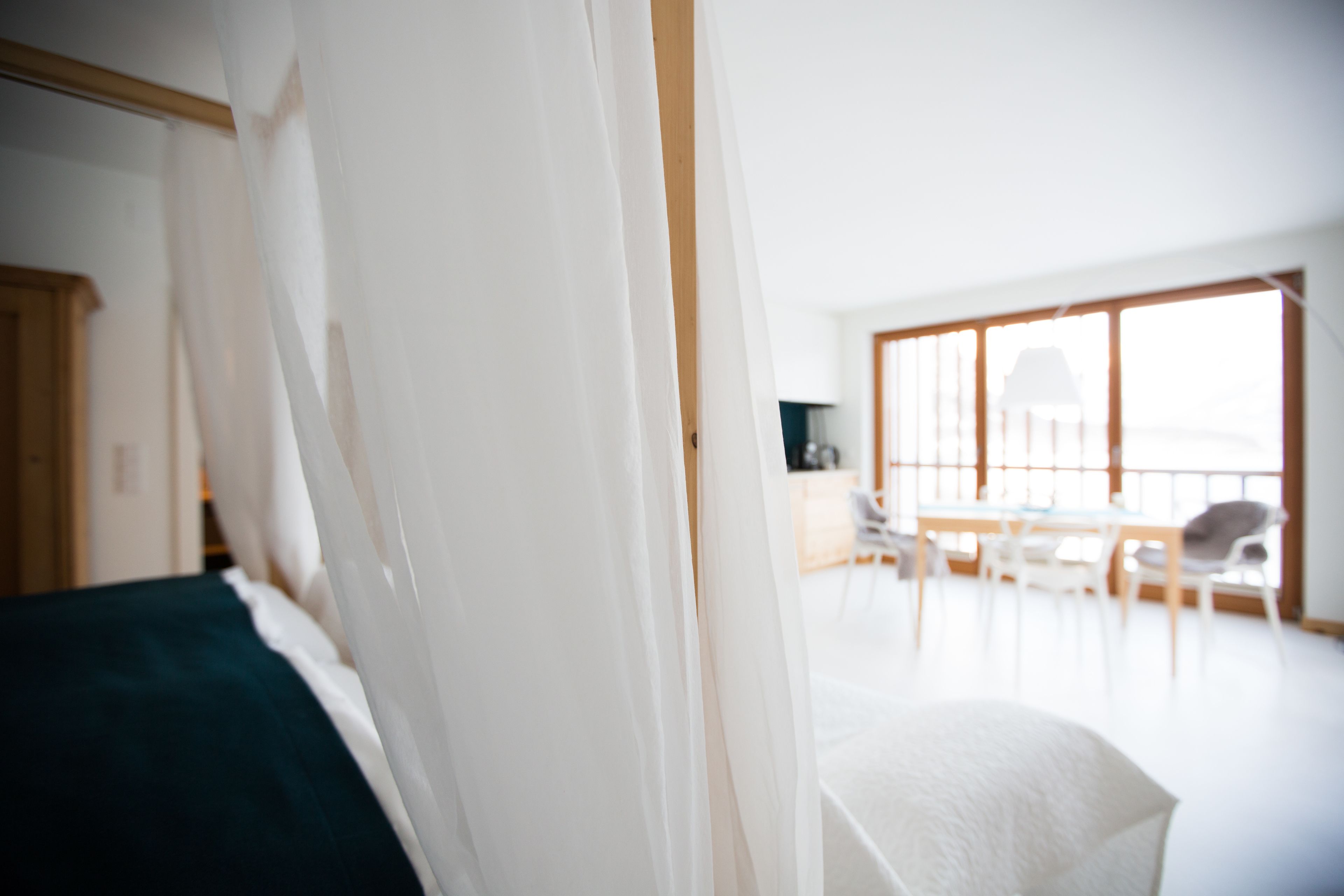 A bedroom with a bed, a window, and a view of a dining area.