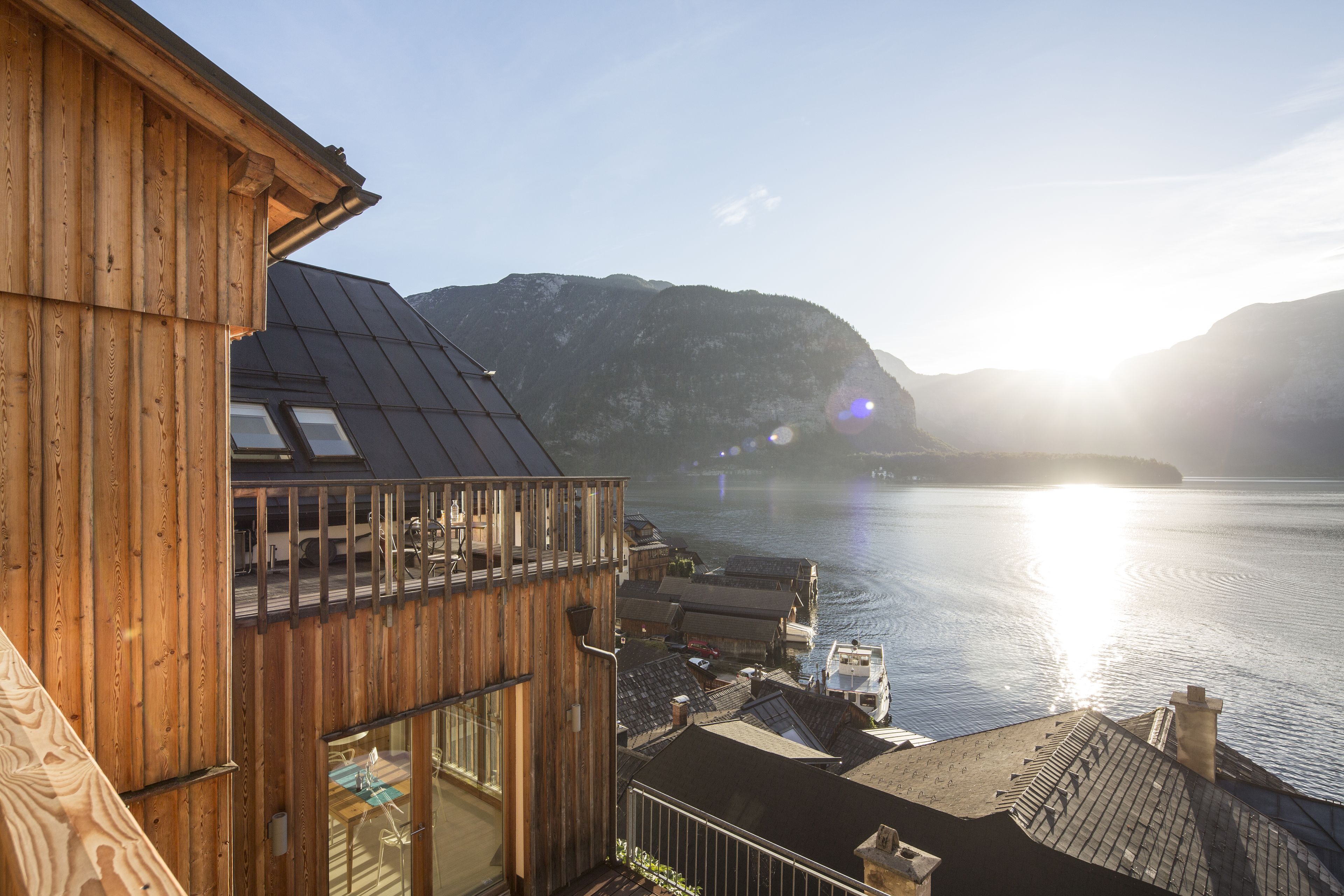 A wooden building with a balcony overlooking a calm body of water and distant mountains.
