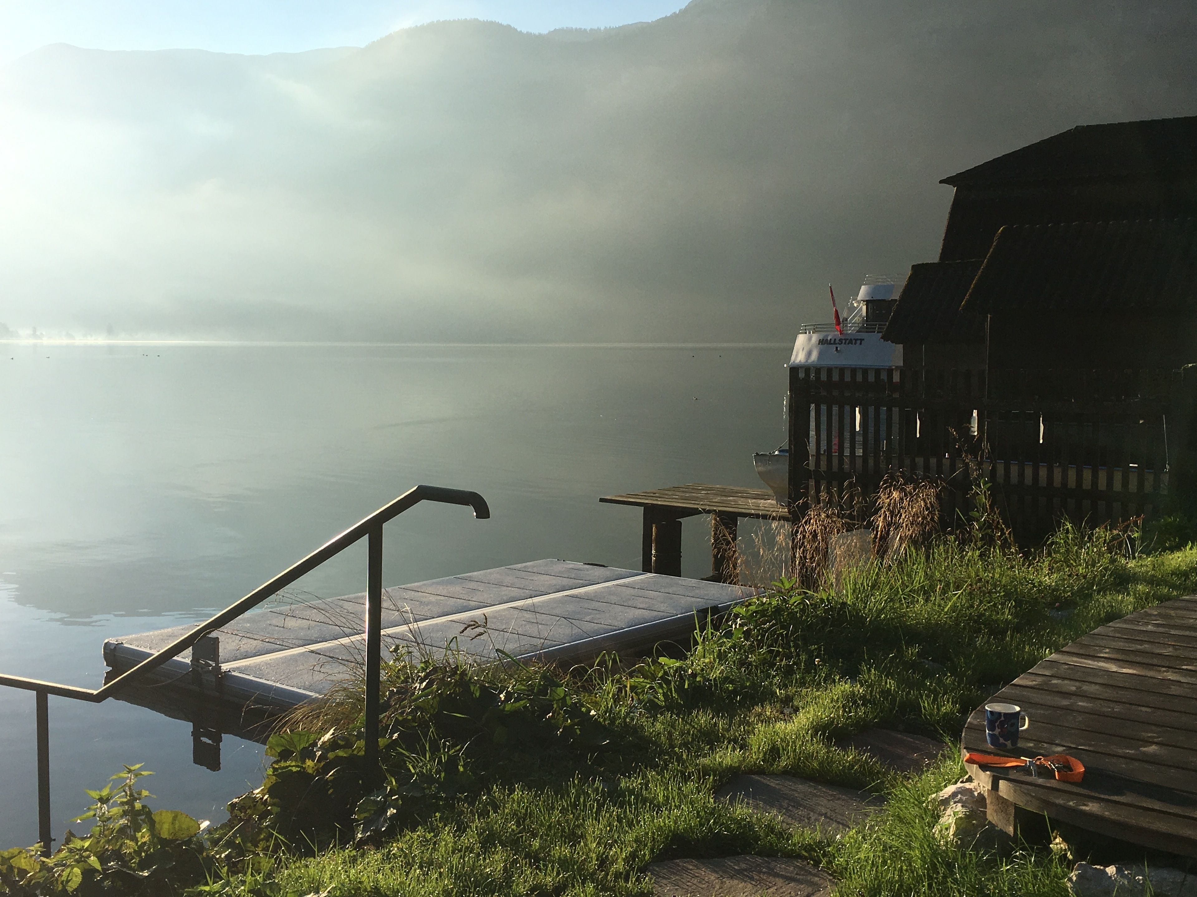 A wooden dock extending into a calm lake with a misty mountain backdrop.