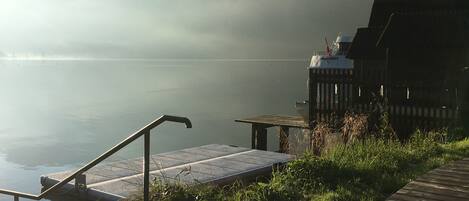 A wooden dock extending into a calm lake with a misty mountain backdrop.