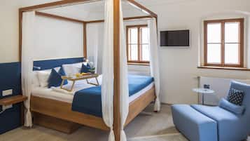 A four-poster bed with a tray of breakfast items, a blue sofa, and a TV on the wall.