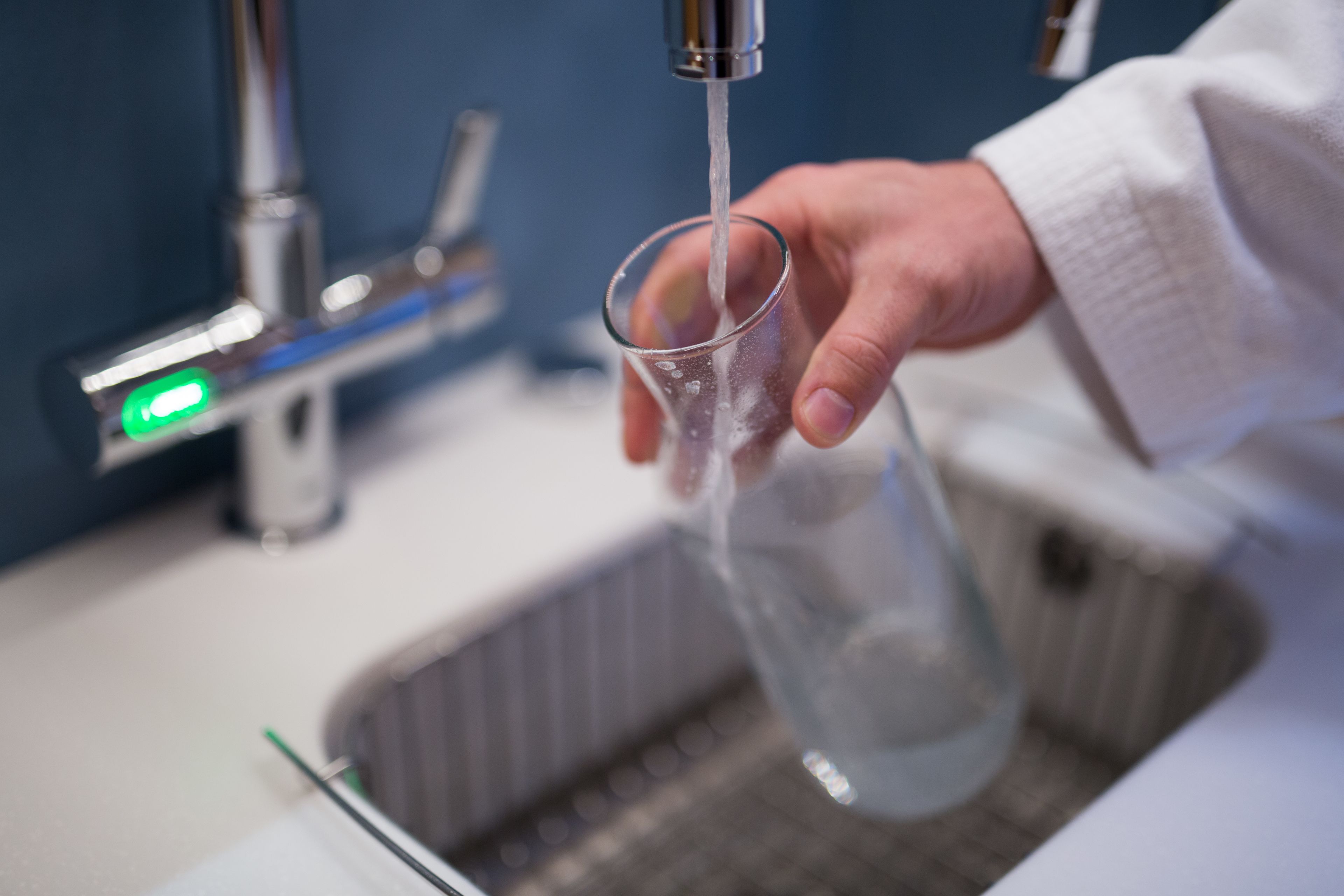 Una mano sosteniendo un vaso debajo de un grifo abierto en un baño.