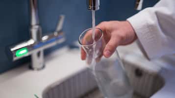 Una mano sosteniendo un vaso debajo de un grifo abierto en un baño.