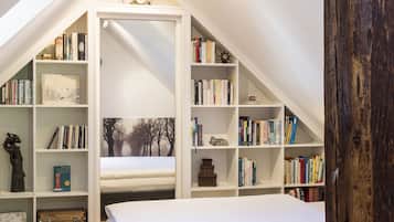 A bedroom with a sloped ceiling, a bed, and built-in bookshelves.