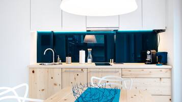 A modern kitchen with a sink, faucet, and a coffee machine. There is a wooden table with chairs and a blue bowl in the center.