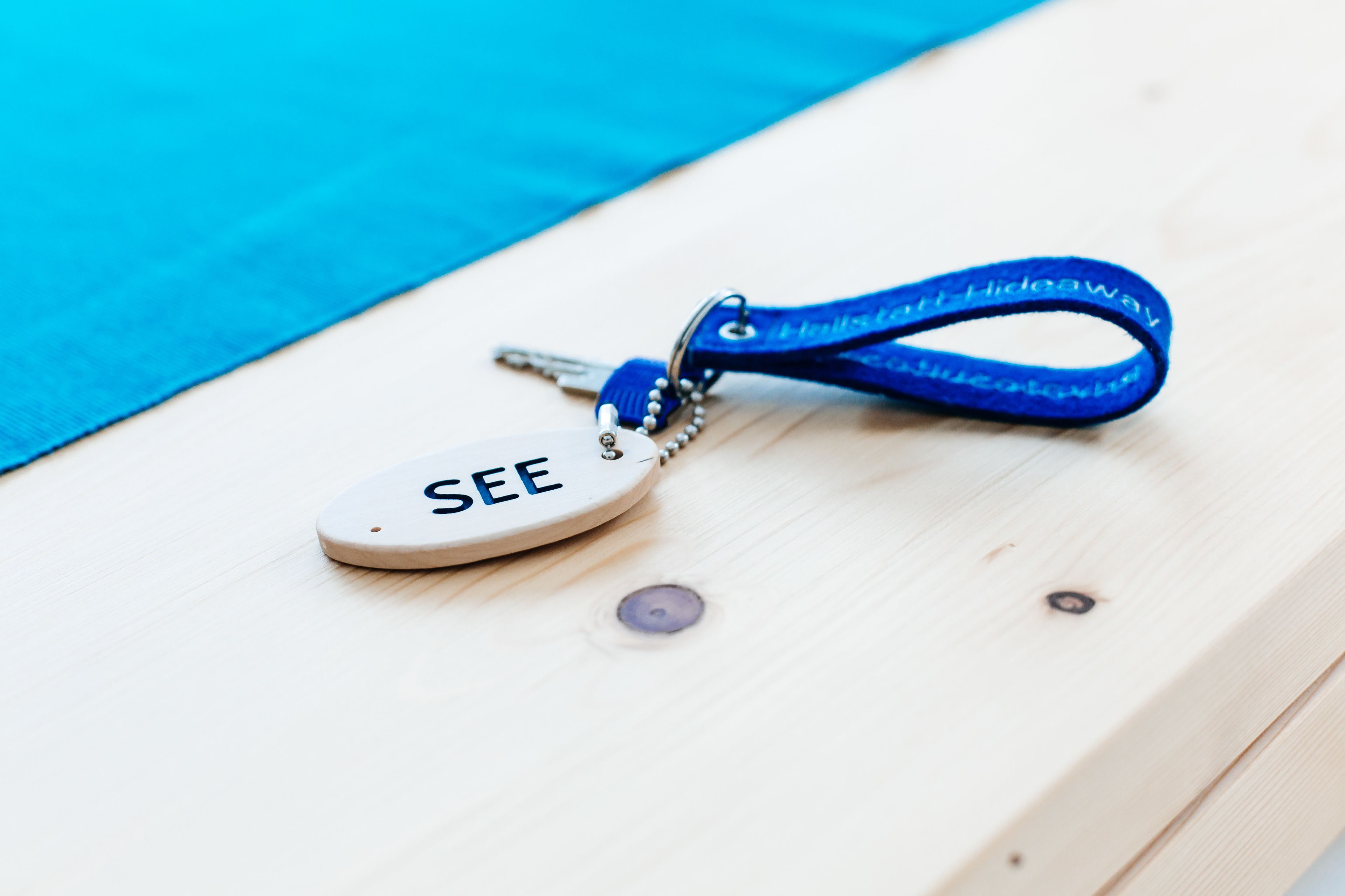 A keychain with the word "SEE" on it, lying on a wooden surface.