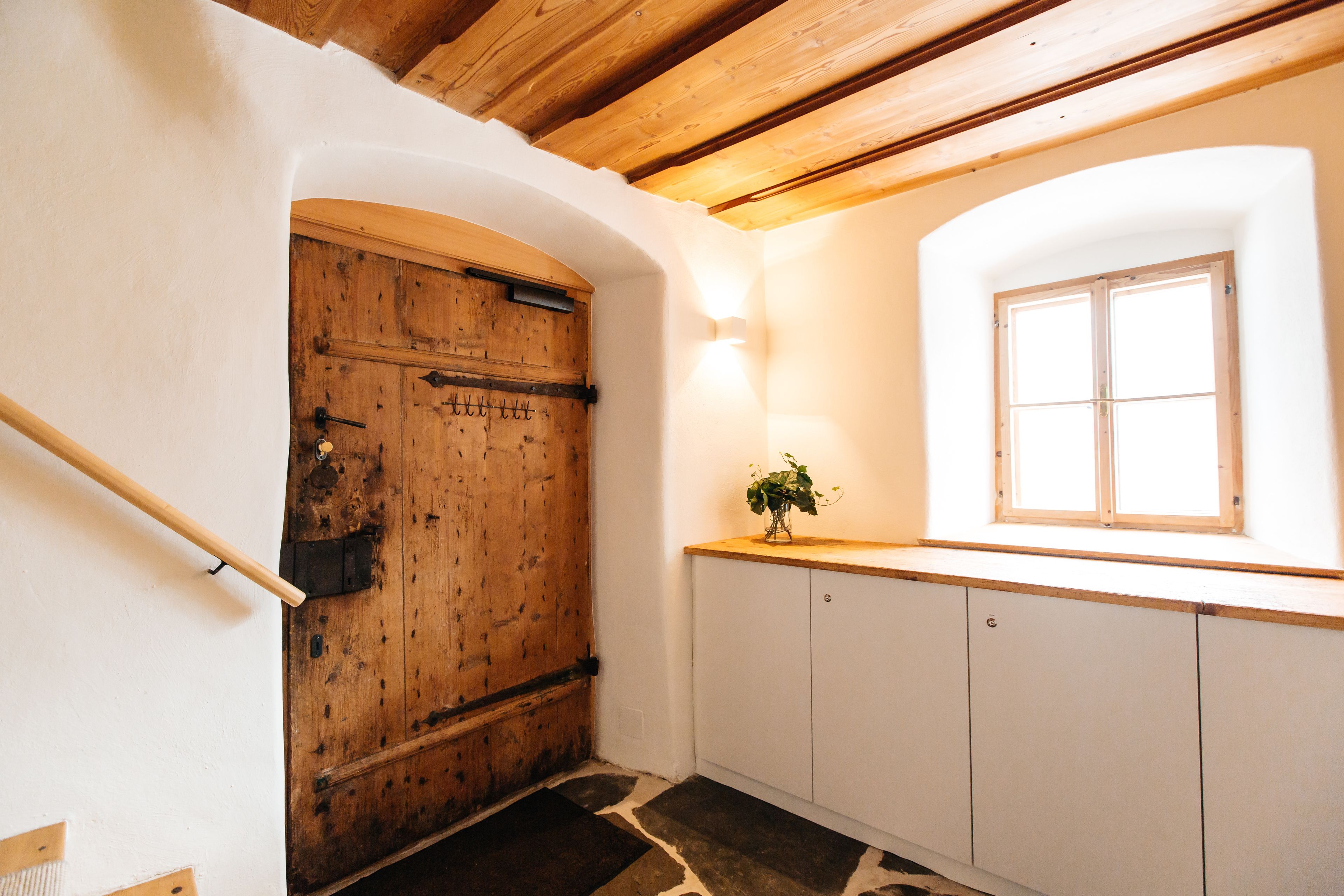 Eine rustikale Küche mit Holztür, weißen Schränken und einem Fenster mit Tageslicht.