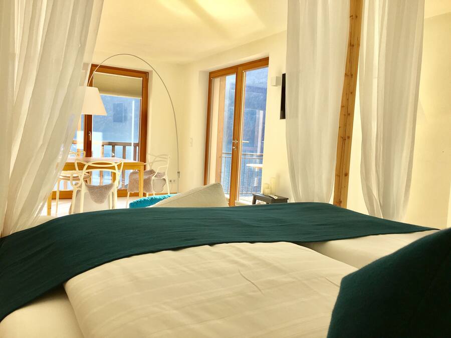 A bedroom with a bed, a chair, a table, and a balcony with a view.