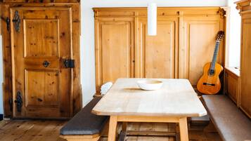 A wooden dining table with a bowl, benches, and a guitar leaning against a wooden cabinet.