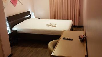 Hotelkamer met een bed, bureau, stoel, nachtkastje, lamp, wandklok en gordijn.