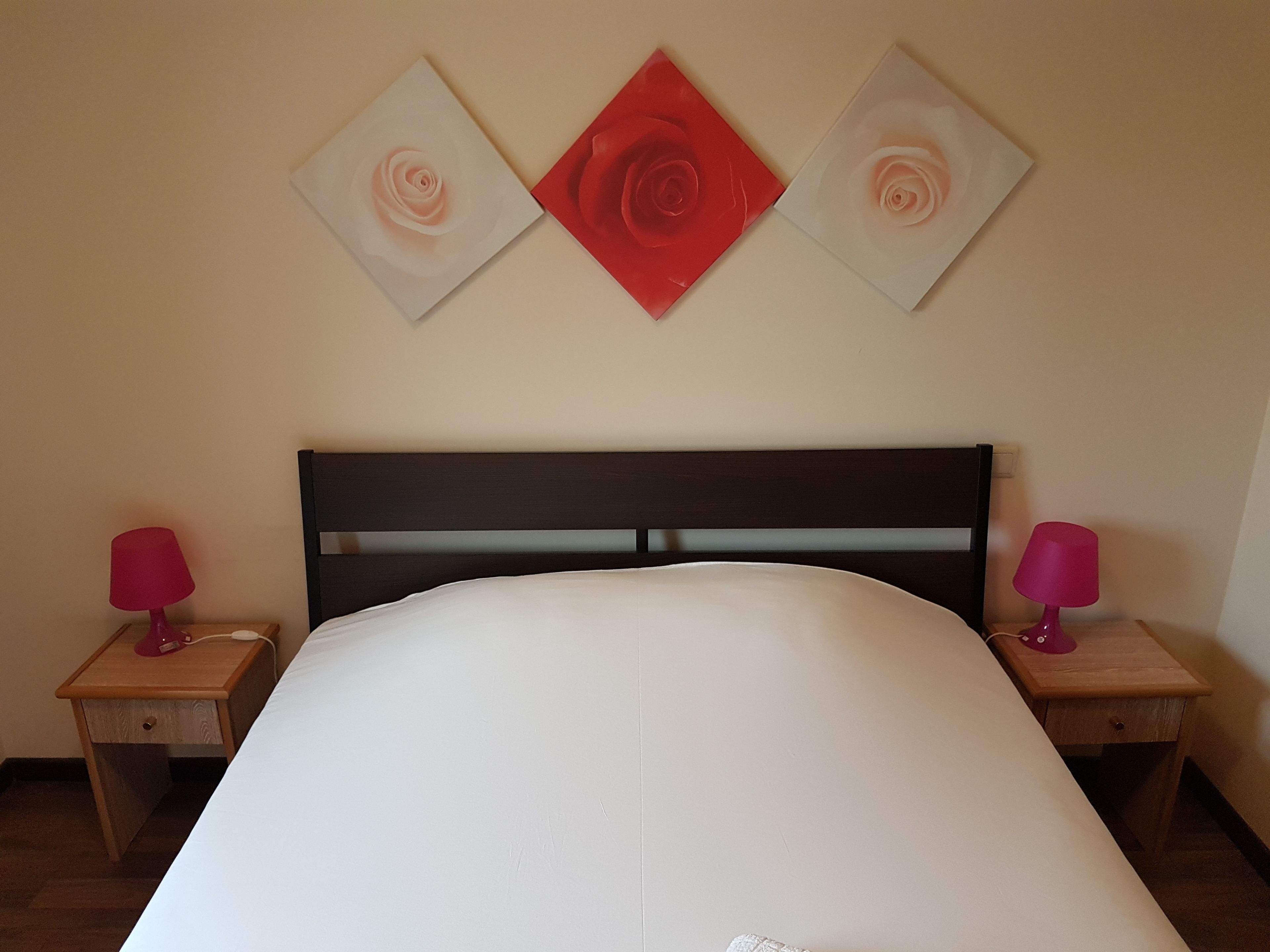 A bedroom with a bed, two bedside tables, and three wall-mounted artworks.