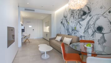 Una sala de estar moderna con una mesa de vidrio, sillas naranjas, un sofá color beige y un mural en la pared.