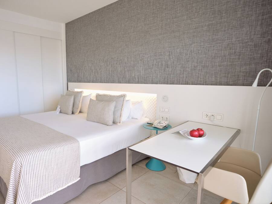Una habitación de hotel con cama, mesita de noche y un pequeño escritorio con un frutero.