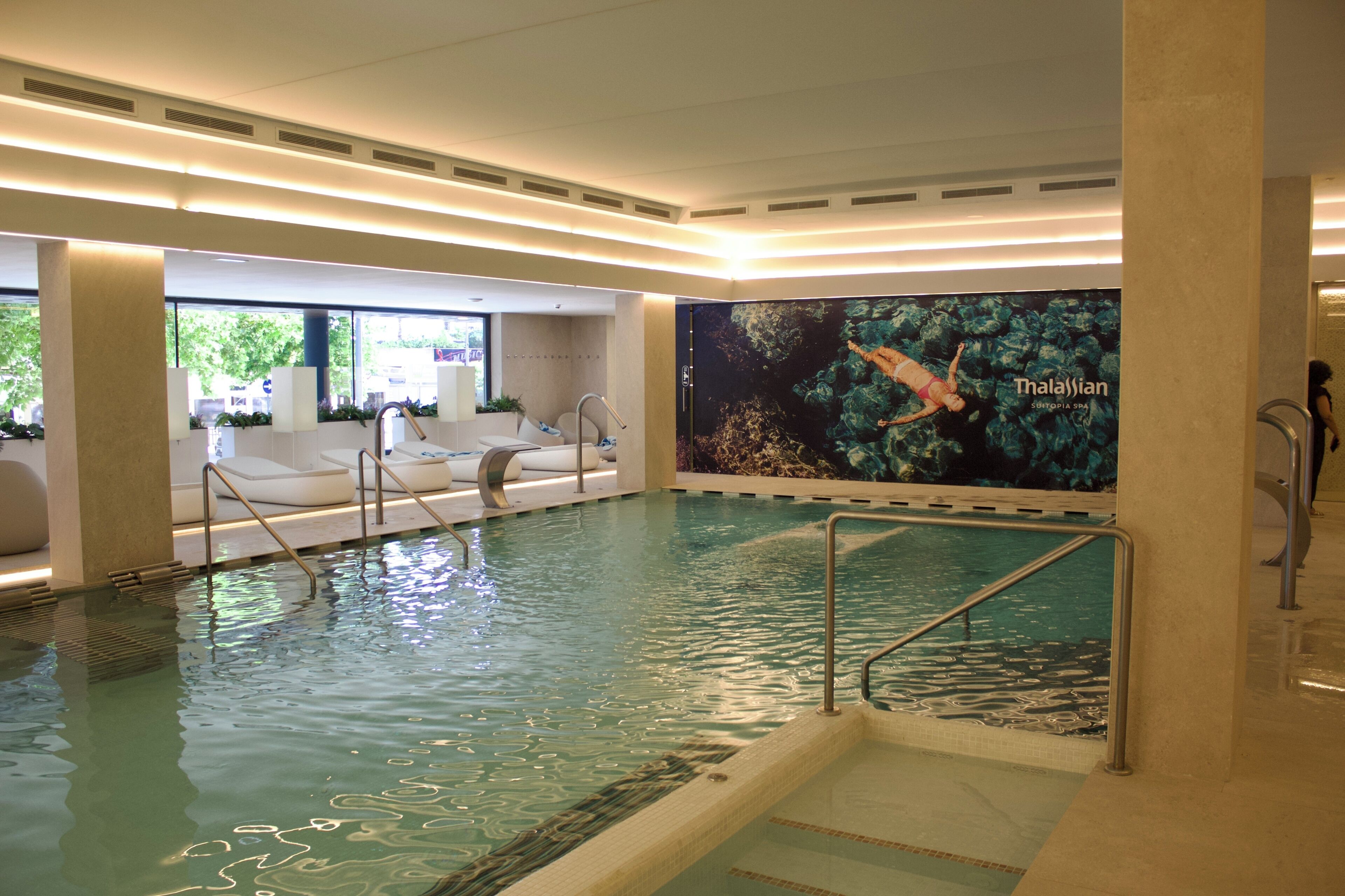 An indoor swimming pool with a mural of a diver, a seating area with loungers, and a spa section.