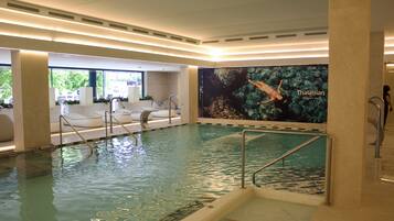 An indoor swimming pool with a mural of a diver, a seating area with loungers, and a spa section.