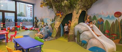 A children's play area with a slide, climbing structures, and colorful tables and chairs.