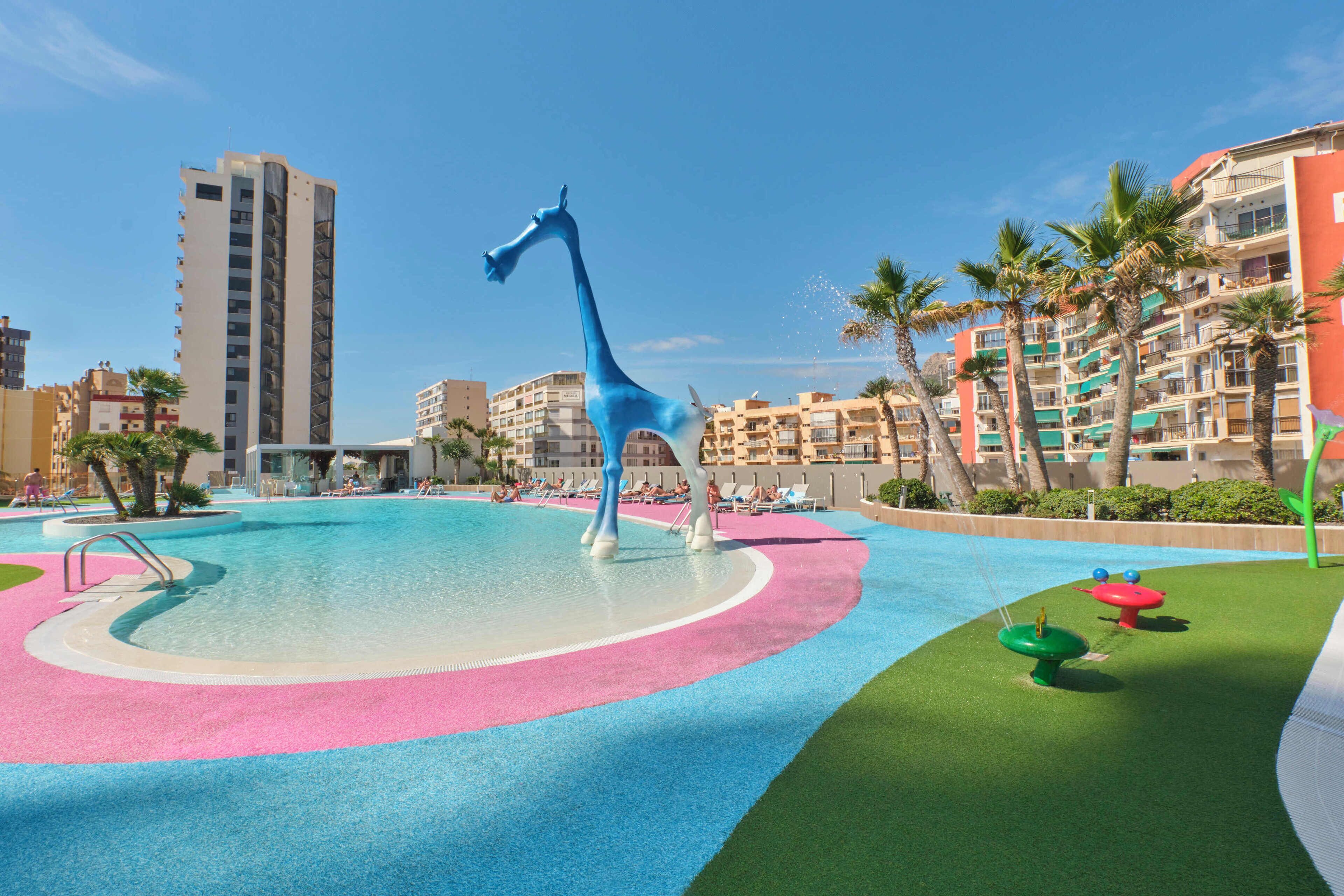 A swimming pool with a giraffe sculpture, surrounded by palm trees and hotel buildings.