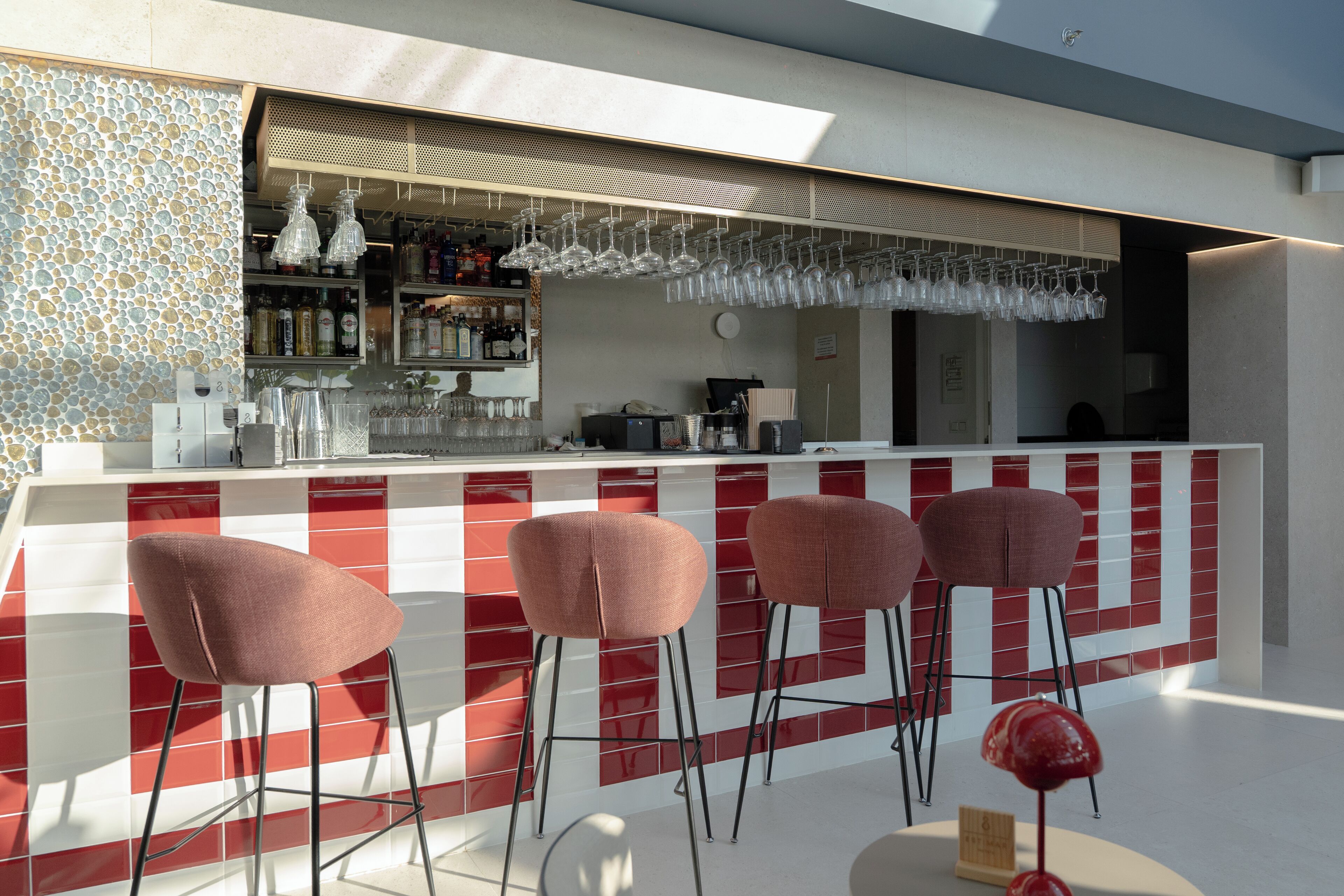 A modern bar area with a red and white tiled backsplash, a bar counter, and four bar stools.