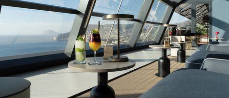 A modern interior with a panoramic ocean view, a round table with drinks, and contemporary seating.