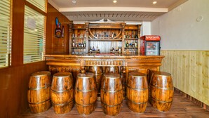 A bar area with wooden bar stools, a variety of liquor bottles, and a Kingfisher Premium vending machine. - Mint Tarika Resort (Kandaghat)