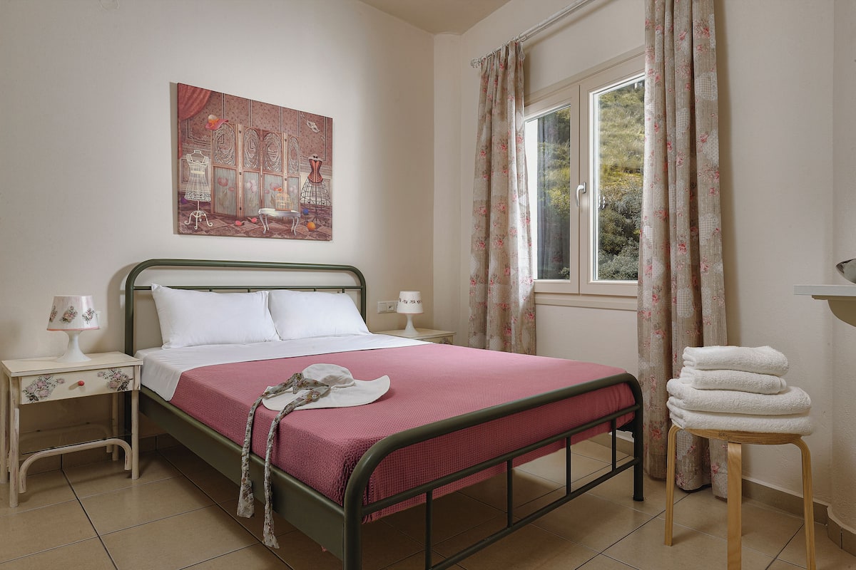 A bedroom with a bed, nightstands, a window with curtains, and a painting on the wall.