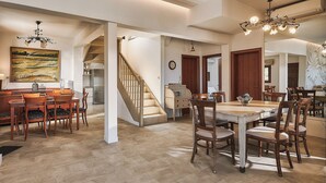 A spacious dining area with a high ceiling, a staircase, and a kitchen in the background. - OZEA - Elevated Living (Malevizi)