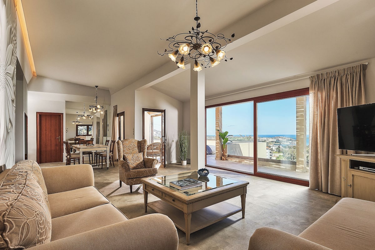 A spacious living room with a large window, a dining area, and a TV.
