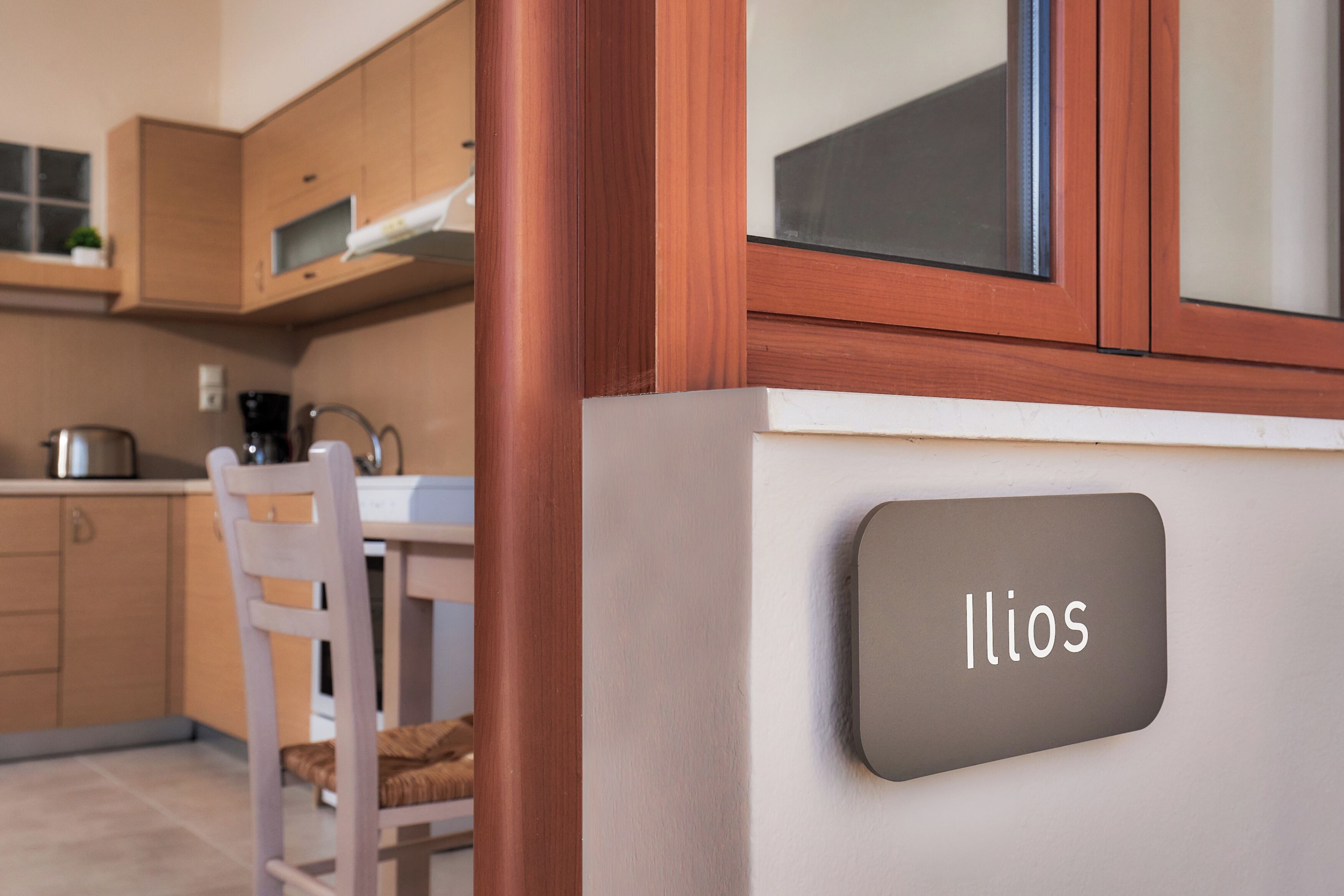 Una cocina moderna con armarios de madera, una silla blanca y una placa con el nombre 'Ilios'.