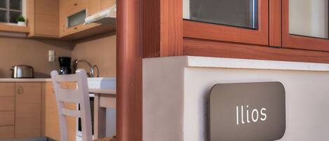 Una cocina moderna con armarios de madera, una silla blanca y una placa con el nombre 'Ilios'.