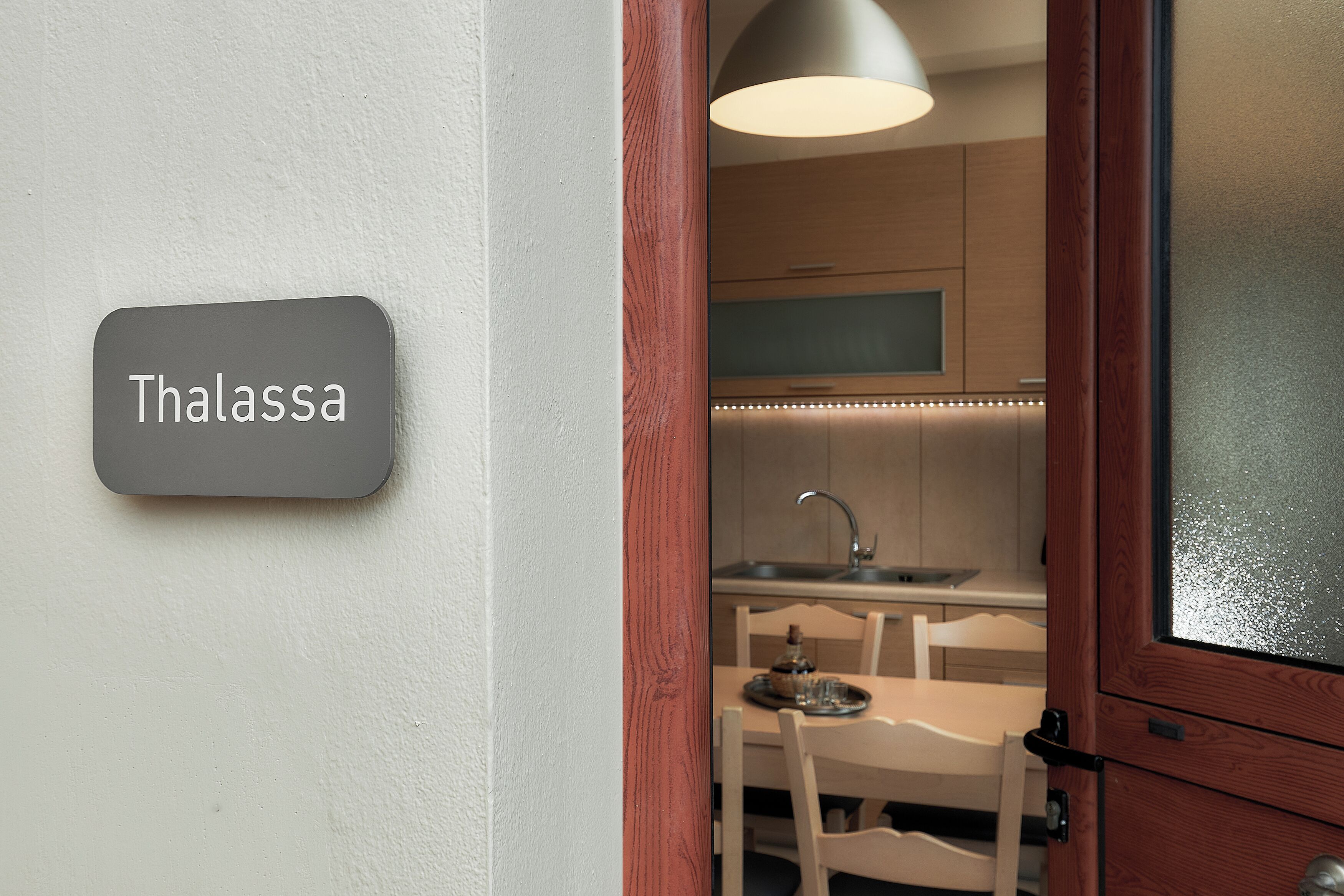 A kitchen with a sink, a dining table with chairs, and a sign that reads 'Thalassa'.