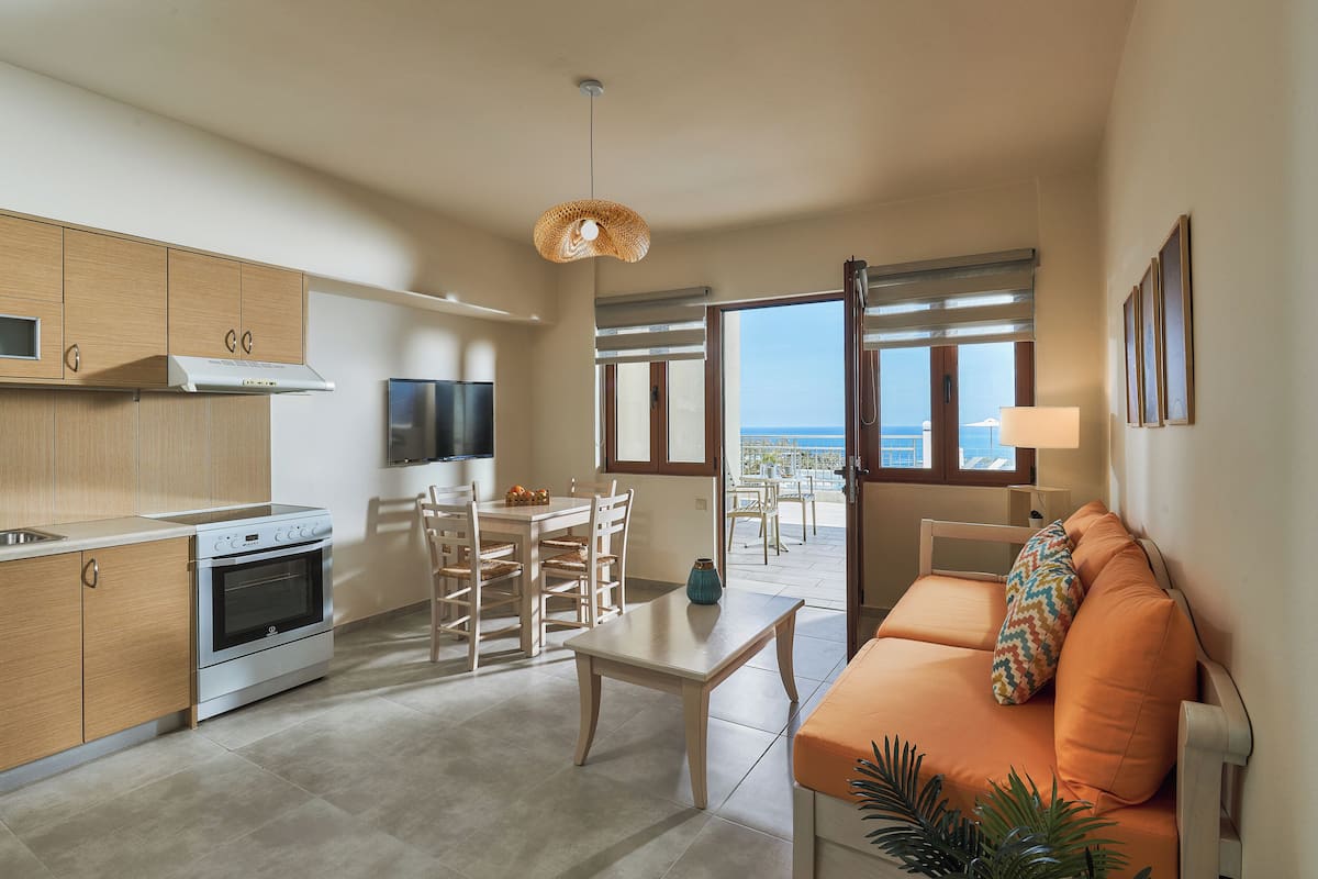 A modern kitchen with a dining area, a sofa, and a view of the sea.