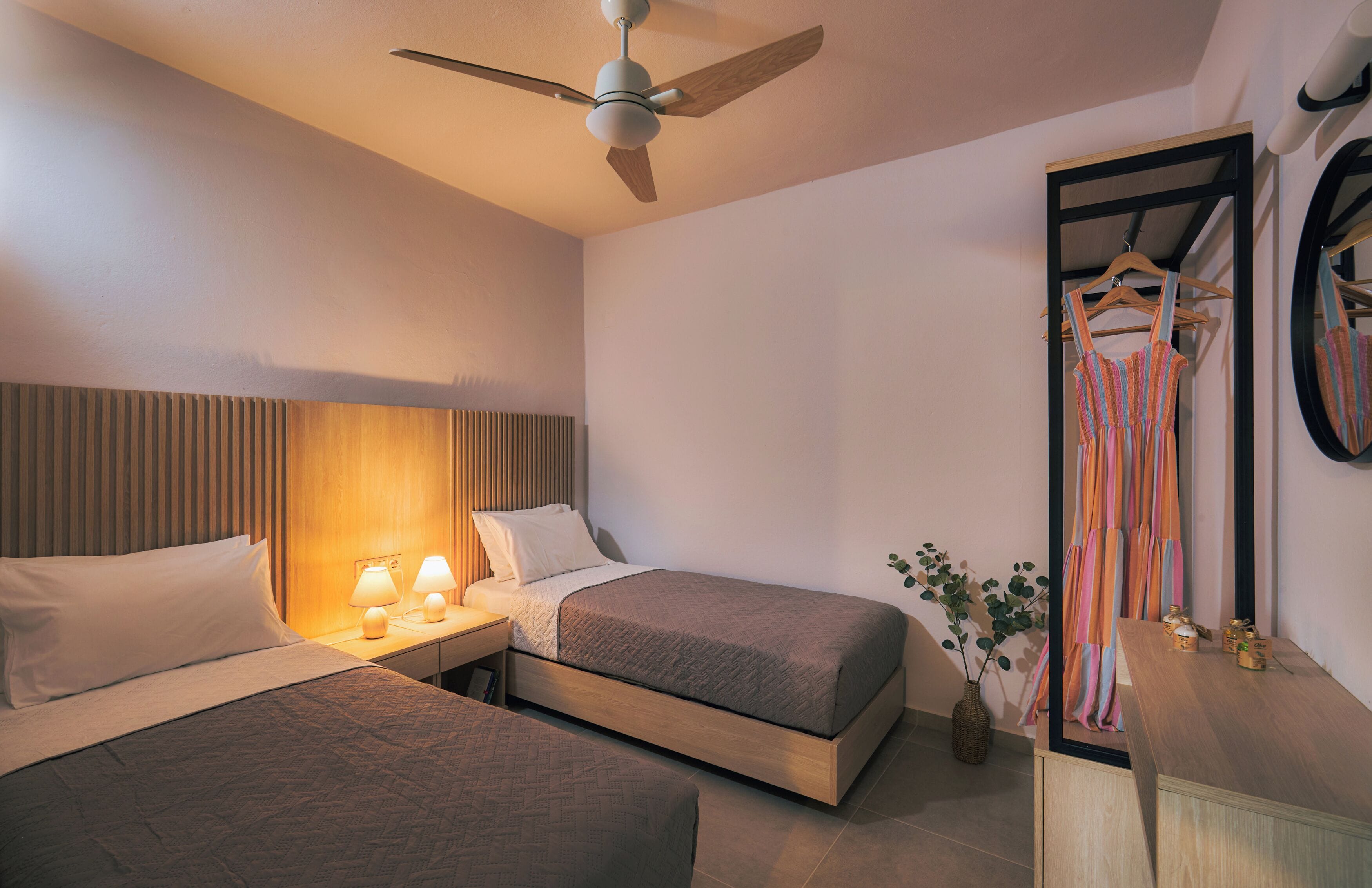 A hotel room with two beds, a ceiling fan, bedside lamps, a mirror, and a dresser.