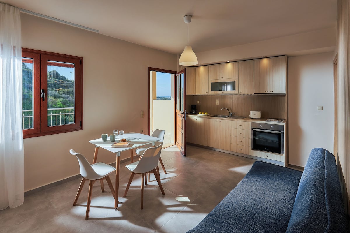 A modern kitchen with wooden cabinets, a dining area with a table and chairs, and a sofa.