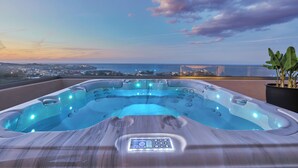 A hot tub with a control panel, surrounded by a wooden deck, overlooking a cityscape and the sea. - OZEA - Elevated Living (Malevizi)