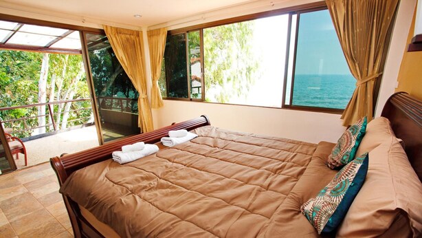 Un dormitorio con una cama grande, vista al mar y un balcón con una silla.