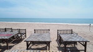 Una playa con mesas y sillas de madera dispuestas sobre la arena, con vista al mar.