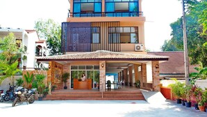 Un hotel de dos pisos con recepción, zona de estar al aire libre y plantas en macetas.