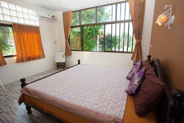 Un dormitorio con una cama grande, una ventana con cortinas, una lámpara de pared y una mesita de noche pequeña.
