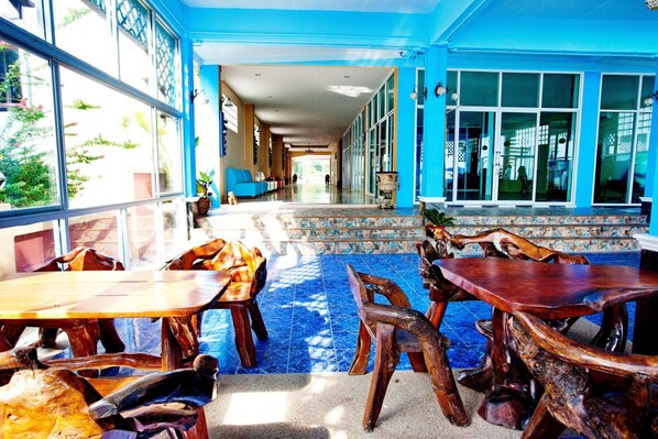 A spacious indoor area with large windows, wooden furniture, and a tiled floor.