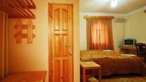 A bedroom with a wooden door, a bed with a patterned bedspread, a small wooden table, and a ceiling fan. - Islambek Hotel & Travel (Khiva)