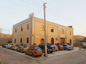 A hotel with a brick facade, multiple windows, and a sign indicating a reception area. Several cars are parked in front. - Islambek Khiva (Khiva)