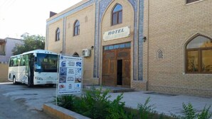 Un hotel con un letrero, un autobús estacionado adelante y un panel de información turística.