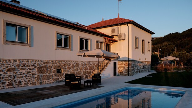 Une maison à deux étages avec une façade en pierre, une piscine, du mobilier d’extérieur et un escalier menant à l’étage supérieur.