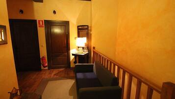 Un pasillo estrecho con un banco de madera, una mesa con lámpara y una puerta con extintor.