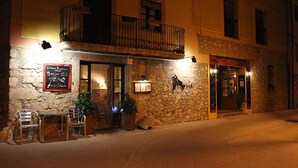 A stone building with a balcony, outdoor seating, and a signboard. - La Fornal dels Ferrers (Terrades)