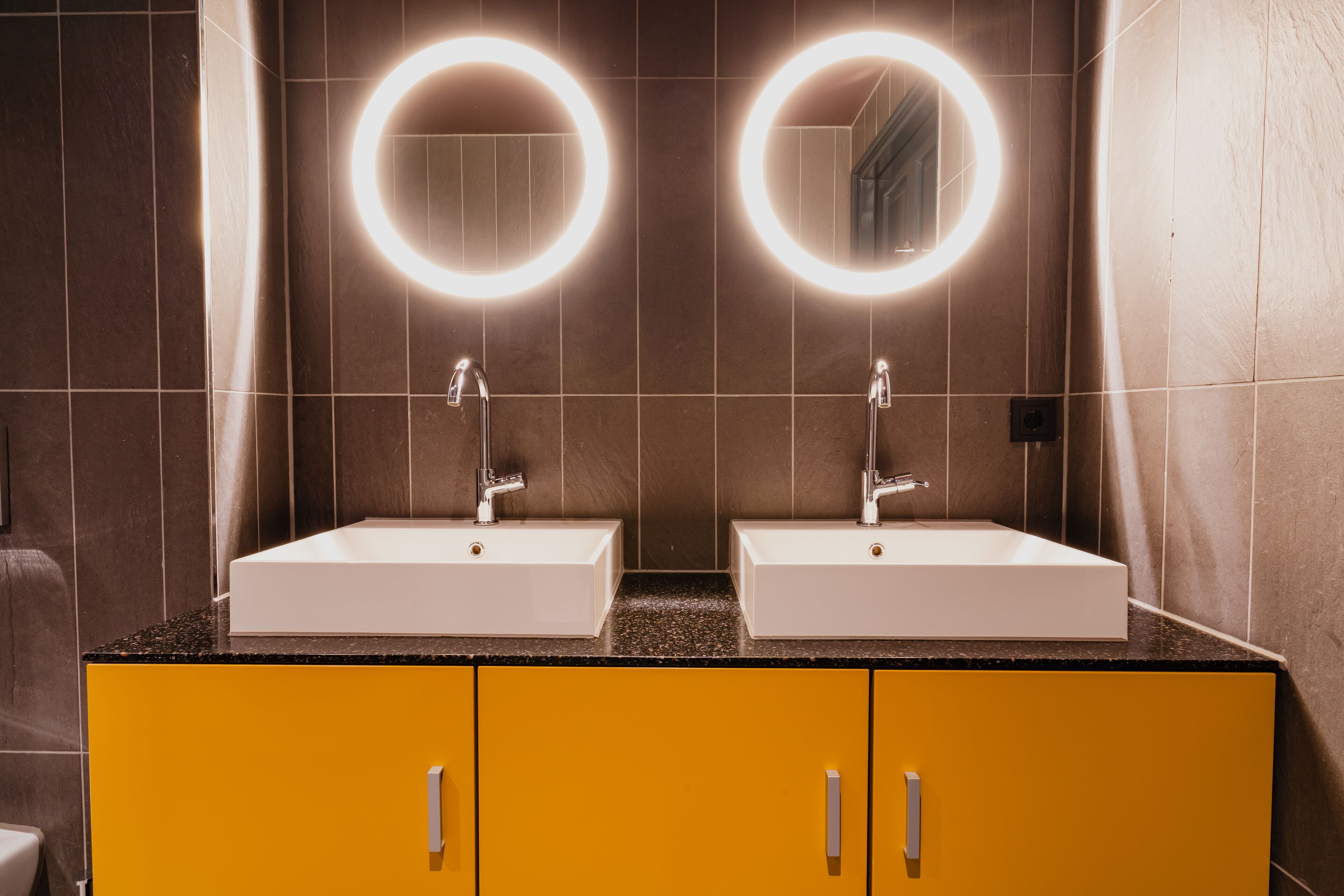 A bathroom with two sinks, each with a round mirror and under-cabinet lighting.